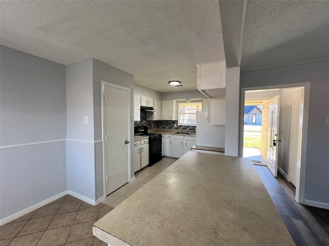 kitchen featuring tasteful backsplash, black range with electric stovetop, a textured ceiling, light tile patterned floors, and white cabinetry