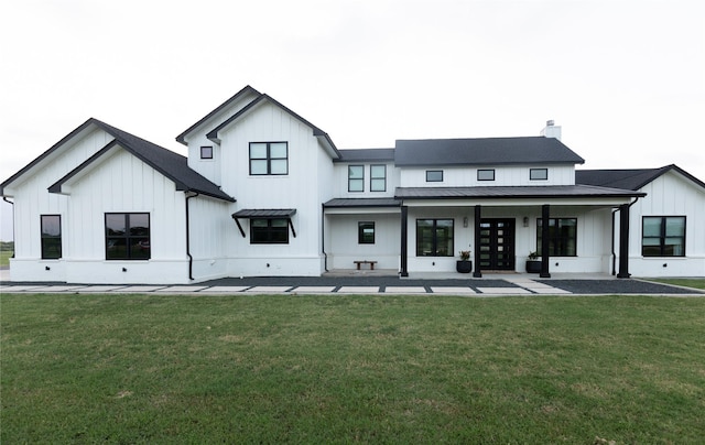 back of house featuring metal roof, a yard, board and batten siding, a standing seam roof, and a chimney