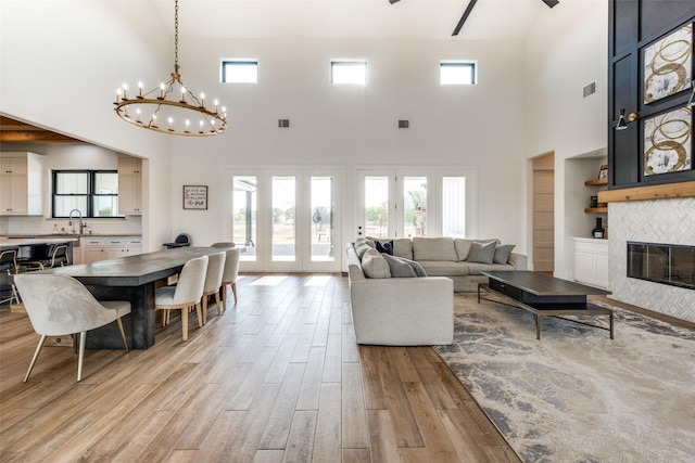 living room featuring light wood-type flooring, sink, a tile fireplace, a notable chandelier, and a high ceiling