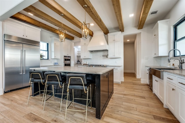 kitchen featuring a center island, custom range hood, stainless steel appliances, and white cabinetry