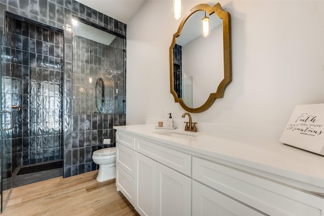 bathroom with tiled shower, hardwood / wood-style flooring, vanity, and toilet