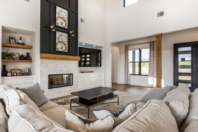 living room featuring a tile fireplace, built in shelves, a high ceiling, and hardwood / wood-style flooring