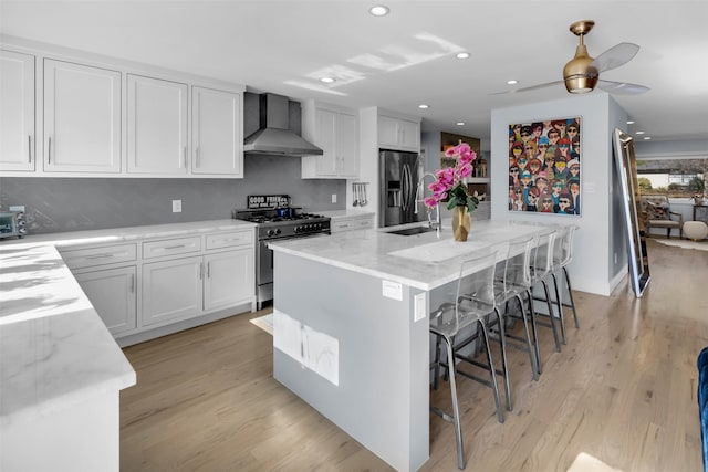 kitchen with white cabinets, stainless steel appliances, wall chimney exhaust hood, and a kitchen island with sink