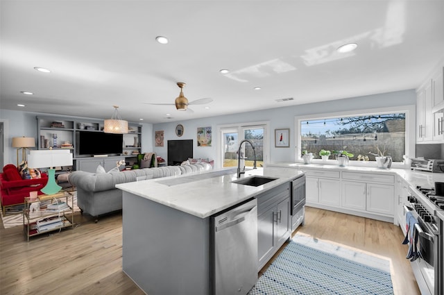 kitchen with ceiling fan, sink, a kitchen island with sink, stainless steel appliances, and white cabinets