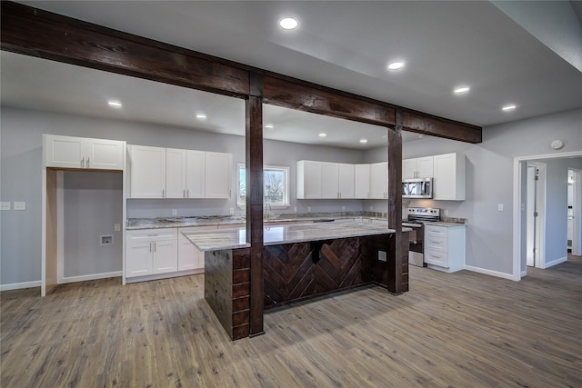 kitchen with light stone countertops, appliances with stainless steel finishes, a kitchen island, wood-type flooring, and white cabinetry