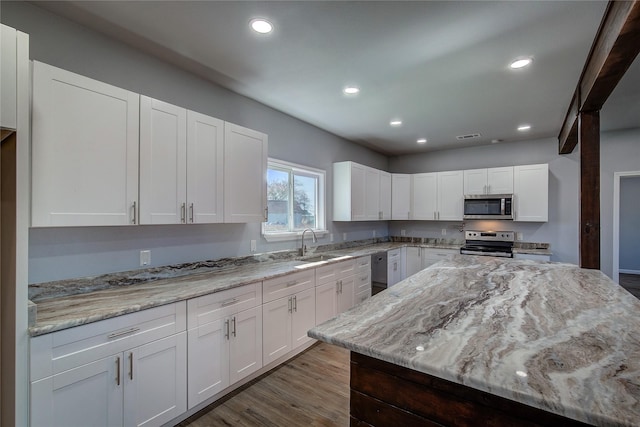 kitchen featuring light stone countertops, sink, hardwood / wood-style floors, white cabinets, and appliances with stainless steel finishes