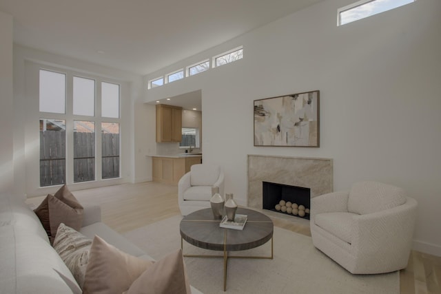 living room featuring plenty of natural light, a premium fireplace, a high ceiling, and light hardwood / wood-style flooring