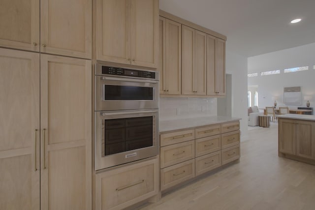 kitchen featuring light wood-type flooring, stainless steel double oven, backsplash, and light brown cabinetry