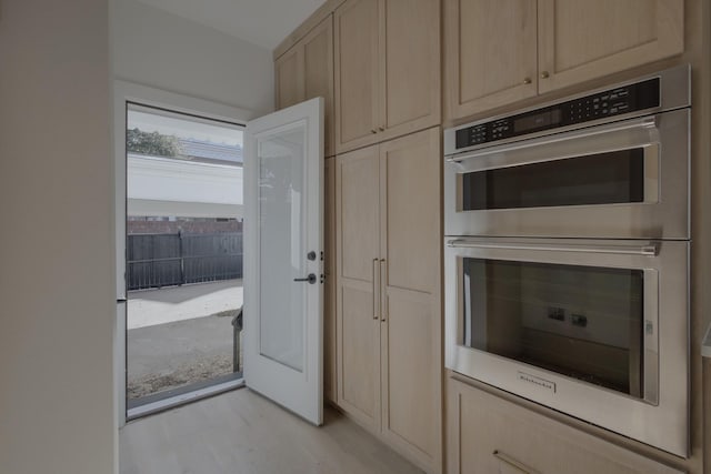 kitchen with light brown cabinets, double oven, and light hardwood / wood-style flooring