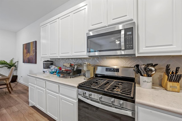 kitchen with tasteful backsplash, white cabinetry, stainless steel appliances, and light hardwood / wood-style floors