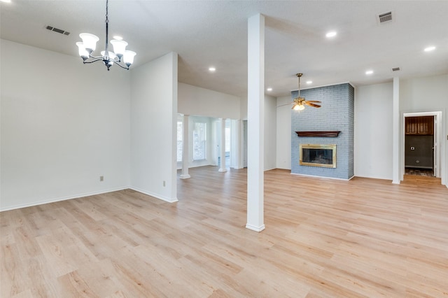 unfurnished living room featuring ornate columns, light hardwood / wood-style flooring, ceiling fan with notable chandelier, and a brick fireplace