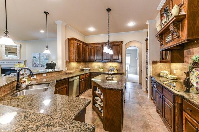 kitchen featuring dishwasher, sink, dark stone countertops, hanging light fixtures, and a center island with sink