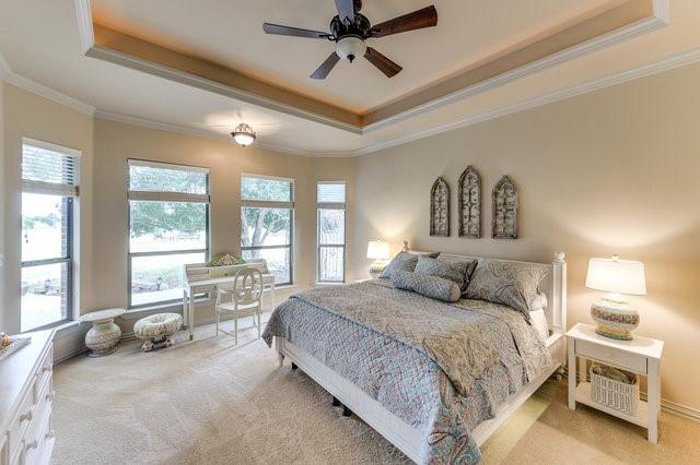 carpeted bedroom with crown molding, ceiling fan, and a tray ceiling