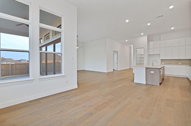 kitchen featuring white cabinetry, backsplash, a kitchen island with sink, ceiling fan, and light hardwood / wood-style floors