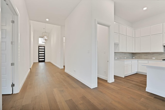 kitchen with decorative light fixtures, a notable chandelier, light hardwood / wood-style floors, decorative backsplash, and white cabinetry