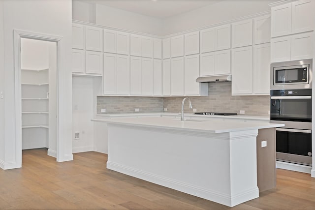 kitchen featuring tasteful backsplash, white cabinetry, sink, stainless steel appliances, and a center island with sink