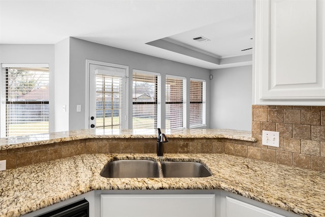 kitchen with decorative backsplash, white cabinetry, sink, and light stone counters