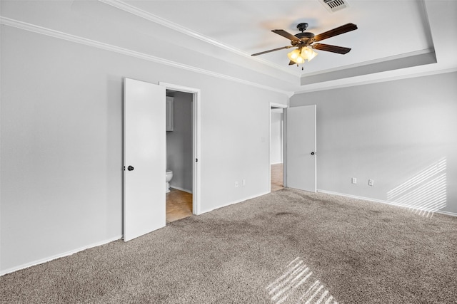 unfurnished bedroom with a raised ceiling, connected bathroom, ceiling fan, and carpet flooring