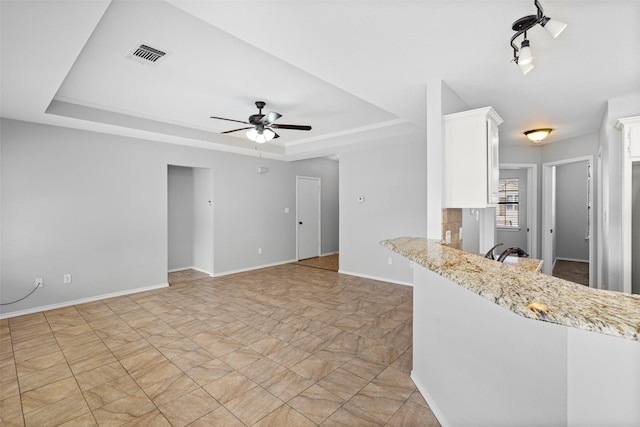 kitchen with white cabinets, ceiling fan, light stone counters, and a tray ceiling