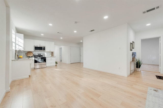 kitchen with tasteful backsplash, light hardwood / wood-style floors, white cabinetry, appliances with stainless steel finishes, and light stone counters