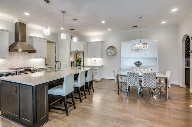 kitchen featuring wall chimney exhaust hood, white cabinetry, hanging light fixtures, appliances with stainless steel finishes, and a large island