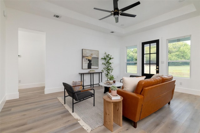 living room featuring ceiling fan, light hardwood / wood-style floors, and a tray ceiling