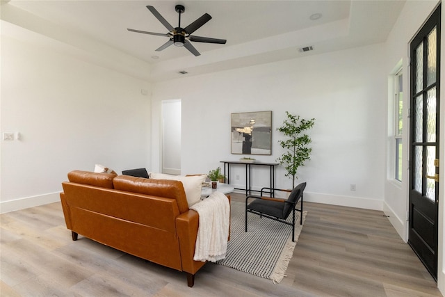 living room with ceiling fan, a raised ceiling, and light wood-type flooring