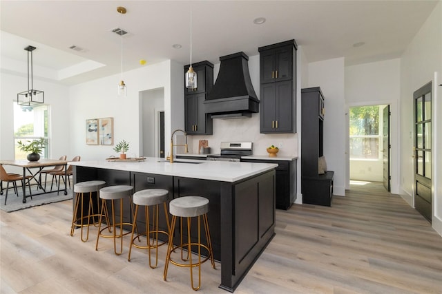 kitchen featuring custom range hood, sink, stainless steel range oven, hanging light fixtures, and an island with sink