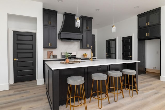 kitchen with a kitchen island with sink, stainless steel gas range, decorative light fixtures, and custom exhaust hood