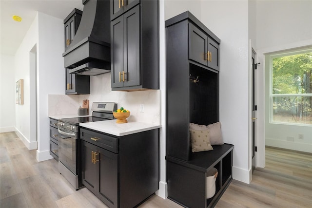 kitchen featuring stainless steel range, light wood-type flooring, backsplash, and custom exhaust hood