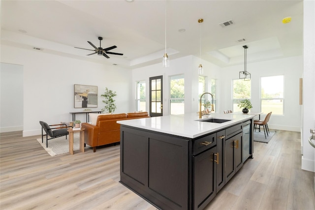 kitchen with a tray ceiling, hanging light fixtures, a center island with sink, and sink