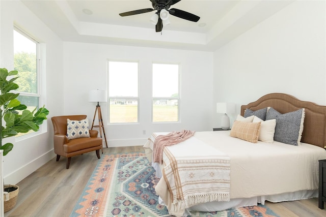 bedroom featuring light hardwood / wood-style flooring, a raised ceiling, and ceiling fan