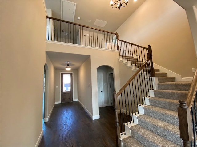 foyer entrance featuring a towering ceiling, baseboards, arched walkways, and wood finished floors