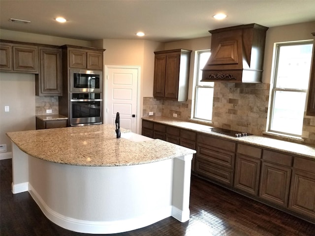 kitchen with a center island with sink, custom range hood, backsplash, appliances with stainless steel finishes, and sink