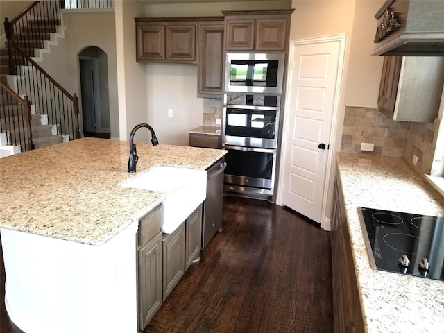 kitchen with tasteful backsplash, light stone counters, and a center island with sink