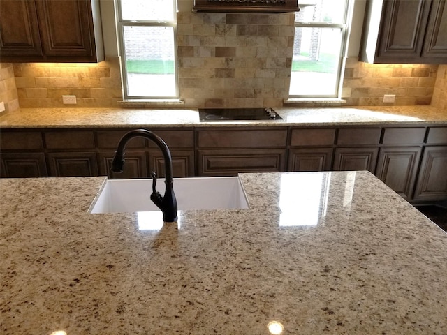 kitchen featuring light stone countertops, electric stovetop, backsplash, and sink