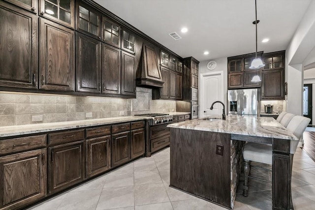 kitchen with a kitchen bar, custom range hood, stainless steel appliances, pendant lighting, and a center island with sink