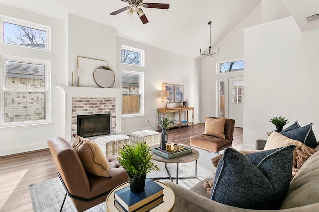 living room featuring hardwood / wood-style floors, a brick fireplace, high vaulted ceiling, and ceiling fan with notable chandelier