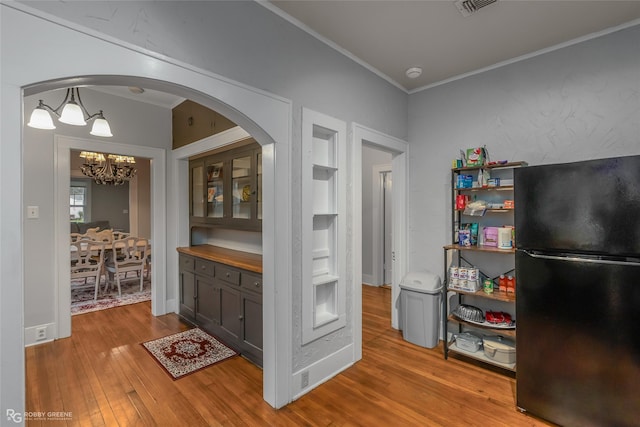 interior space featuring light wood-type flooring, ornamental molding, a chandelier, and black fridge