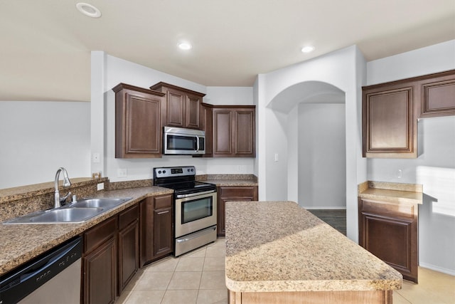 kitchen with appliances with stainless steel finishes, dark brown cabinetry, sink, light tile patterned floors, and a center island