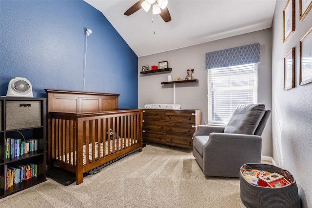 carpeted bedroom featuring lofted ceiling, a crib, and ceiling fan