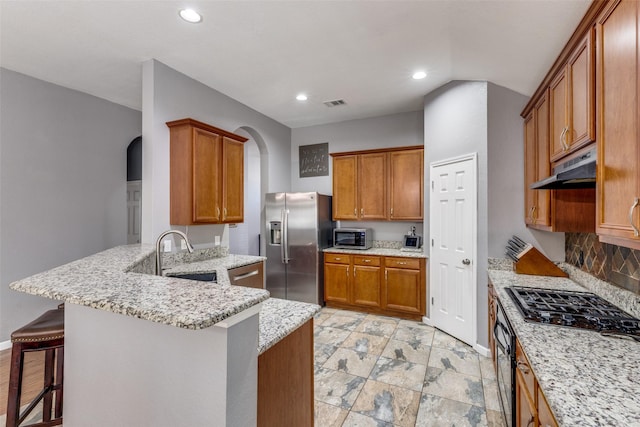 kitchen with a kitchen bar, sink, light stone counters, appliances with stainless steel finishes, and kitchen peninsula