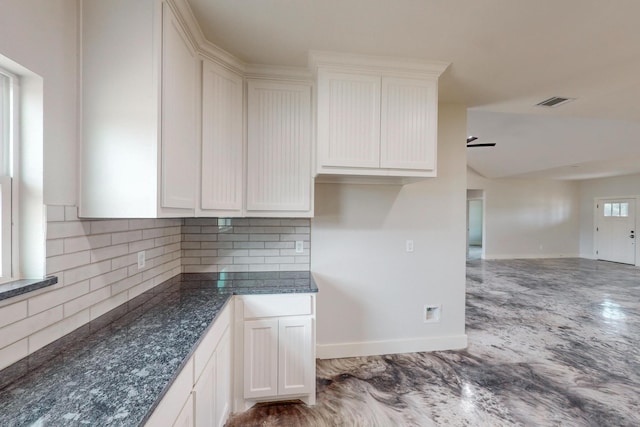 kitchen featuring decorative backsplash, white cabinetry, ceiling fan, and dark stone counters