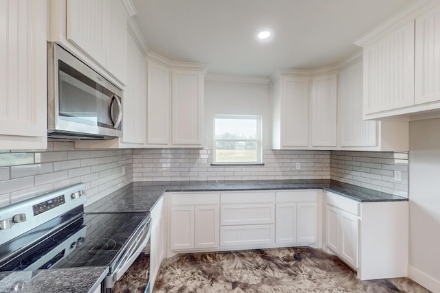 kitchen with appliances with stainless steel finishes, backsplash, ornamental molding, dark stone countertops, and white cabinets