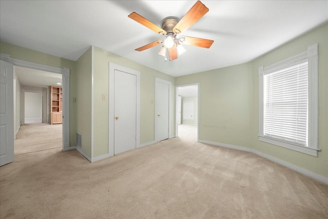 unfurnished bedroom with ceiling fan, light colored carpet, and two closets