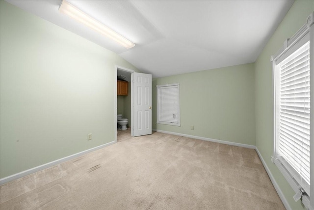 unfurnished bedroom with vaulted ceiling, light carpet, and ensuite bath