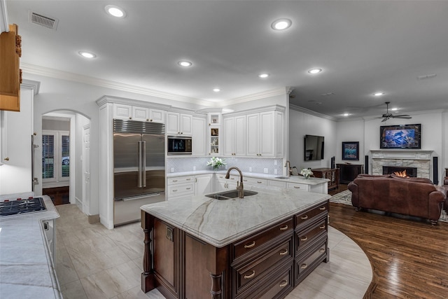 kitchen with sink, white cabinetry, light stone counters, built in appliances, and a center island with sink