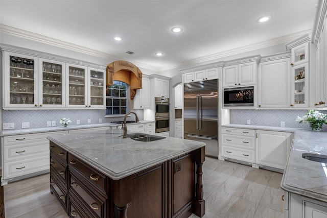 kitchen featuring white cabinetry, sink, built in appliances, and an island with sink