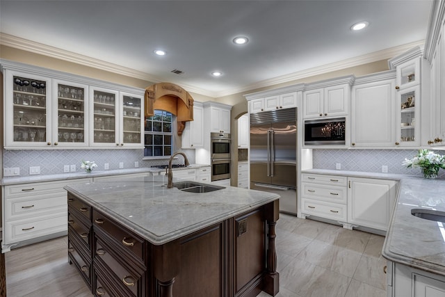 kitchen with white cabinetry, built in appliances, sink, and a center island with sink