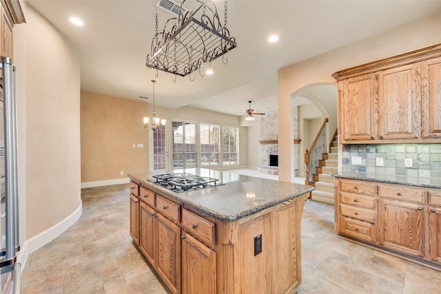 kitchen featuring stainless steel gas stovetop, a center island, ceiling fan with notable chandelier, decorative backsplash, and a fireplace